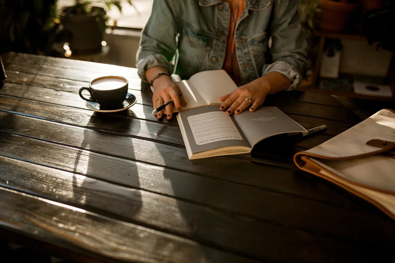 Person writing in a notebook beside a cup of coffee