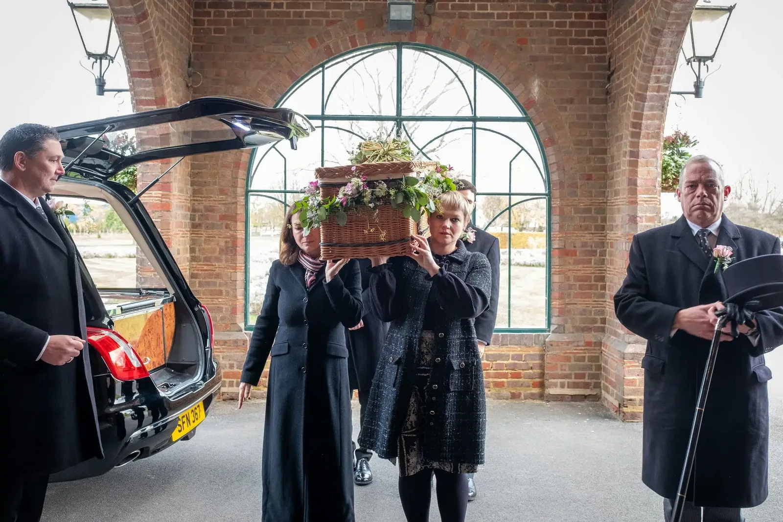 Pallbearers carrying a casket with flowers at a funeral service